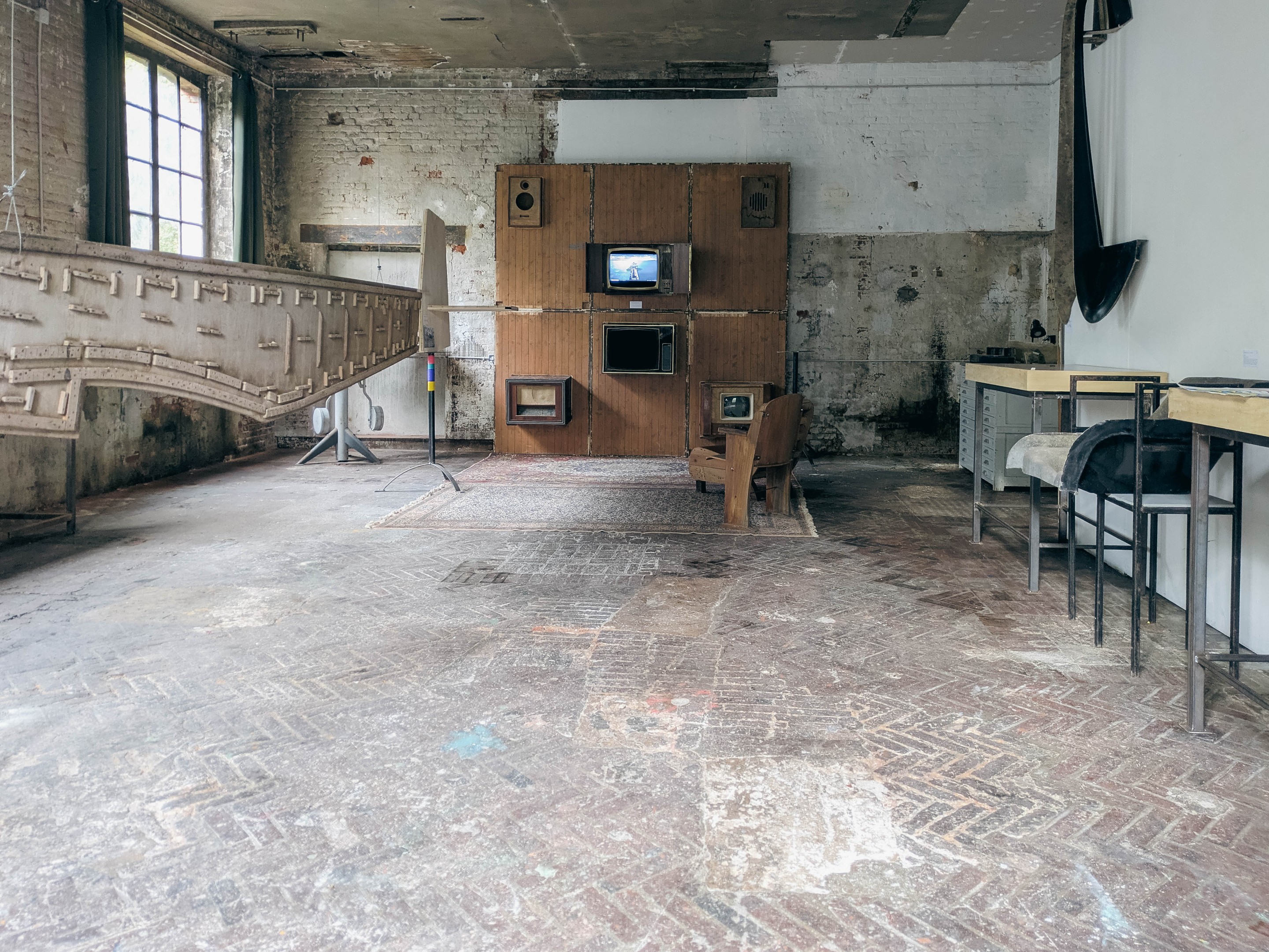 Salle d’exposition : profil d’avion suspendu à gauche, mur de téléviseurs au fond, tables d’archives à droite
